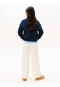 Pull en laine bleu marine avec un motif texturé, ourlet rayé bleu clair, associé à un pantalon large blanc et des baskets beiges.