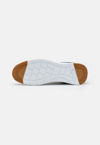 Shoe sole with a white, textured rubber surface and a brown section at the heel, featuring a zigzag pattern for traction.