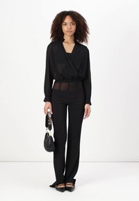 Blusa nera trasparente con maniche lunghe e scollatura a V, abbinata a pantaloni neri aderenti e ballerine con punta. Accentuata da una borsa nera texture.