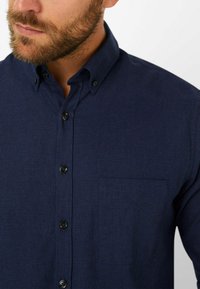 Navy-blaues Hemd aus strukturiertem Stoff mit Button-Down-Kragen, Brusttasche und schwarzen Knöpfen, das ein klassisches Design schafft.
