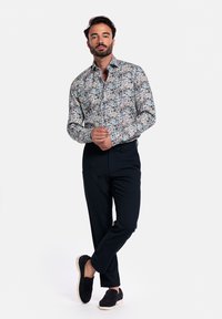 Bloemen overhemd met lange mouwen in blauw, groen en crème patronen. Gecombineerd met donkere broeken en zwarte instap schoenen. Eenvoudig kraagontwerp.