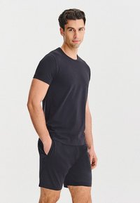Czarny bawełniany t-shirt z okrągłym dekoltem i pasujące szorty. Tkanina wydaje się gładka, o dopasowanym kroju, z bocznymi kieszeniami w szortach.