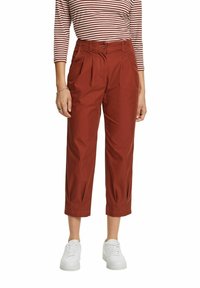 Rode cropped broek met plooien aan de voorkant, een knoopsluiting en een gladde textuur, gecombineerd met witte sneakers en een gestreept top.