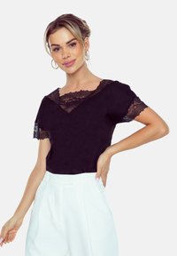 Czarna bluzka z koronkowymi akcentami na dekolcie i rękawach, z krótkimi rękawami i luźnym krojem, połączona z białymi spodniami o wysokim stanie.