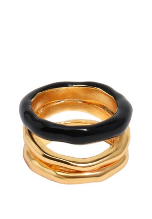 Anillos apilados con formas irregulares, dos anillos de oro en la parte inferior y un anillo negro brillante encima, sobre un fondo blanco.