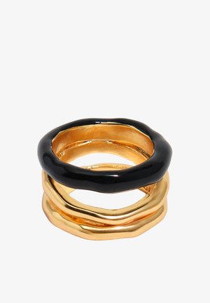Gestapelte Ringe mit unregelmäßigen Formen, zwei goldene Ringe unten und ein glänzender schwarzer Ring oben, vor weißem Hintergrund.
