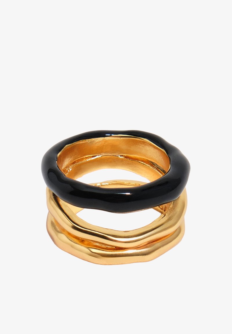 Anneaux empilés aux formes irrégulières, deux anneaux en or en bas et un anneau noir brillant au-dessus, sur fond blanc.