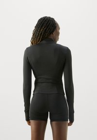 Maglietta nera a maniche lunghe con un design aderente e cuciture piatte, abbinata a pantaloni corti neri. Il tessuto appare liscio ed elastico.