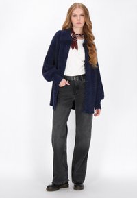 Marineblauwe fluffy cardigan met een kraag, knopen aan de voorkant en losse mouwen, gecombineerd met zwarte denim jeans en zwarte laarzen. Witte t-shirt eronder.