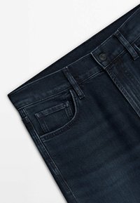 Ceinture de jean en denim bleu foncé montrant un bouton, des passants de ceinture et une poche avant avec une poche à monnaie sur fond blanc.