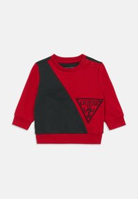 Red and black long-sleeve sweatshirt with a diagonal design, featuring a triangle logo patch and snap buttons on one shoulder.