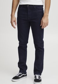 Jeans de mezclilla azul oscuro con corte recto, que cuentan con un cierre frontal de botón y cremallera, diseño clásico de cinco bolsillos y detalles de costura sutiles.
