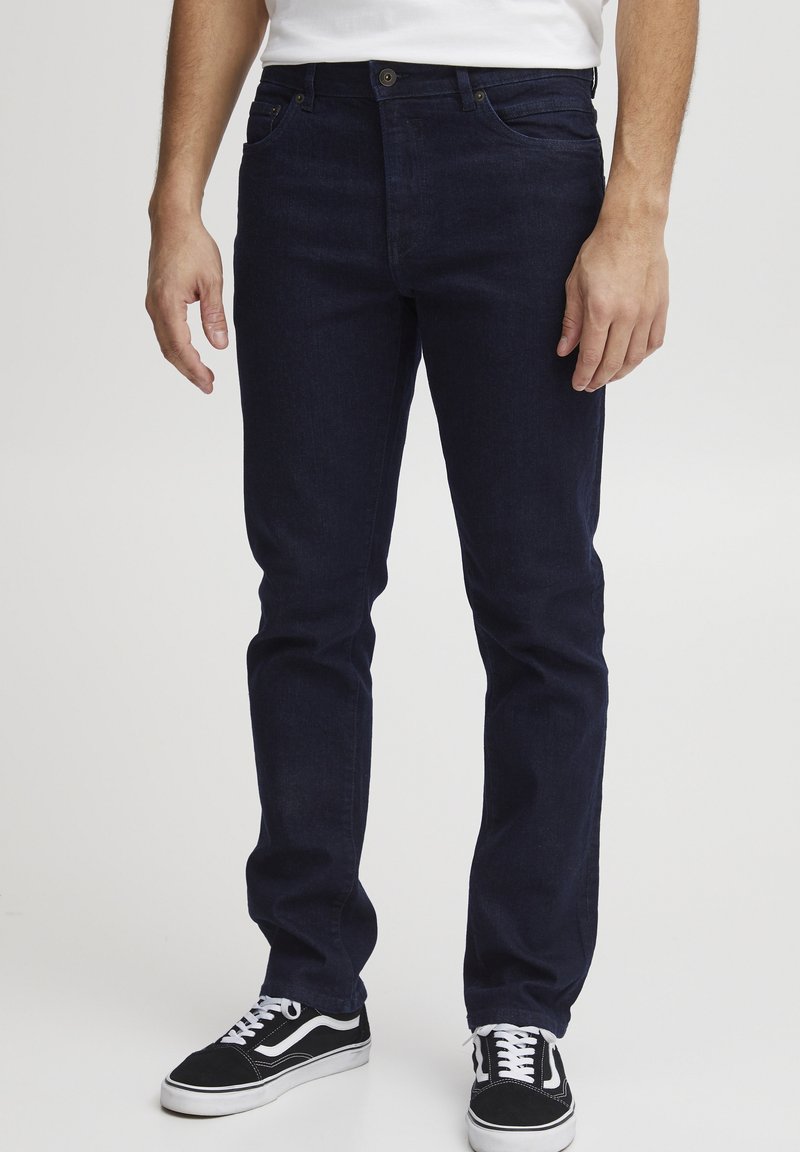 Jeans de mezclilla azul oscuro con corte recto, que cuentan con un cierre frontal de botón y cremallera, diseño clásico de cinco bolsillos y detalles de costura sutiles.