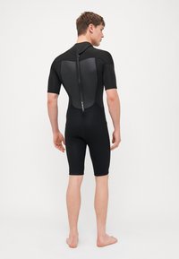 Rövidujjú fekete búvárruha, sima textúrájú, rugalmas dizájnnal, testhezálló formával, hátsó cipzárral és panel kiemelésekkel. Alkalmas vízi sportokhoz.