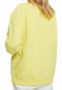 Žlutá oversized mikina s kulatým výstřihem a spadenými rameny. Měkká, texturovaná tkanina a žebrovaný lem.