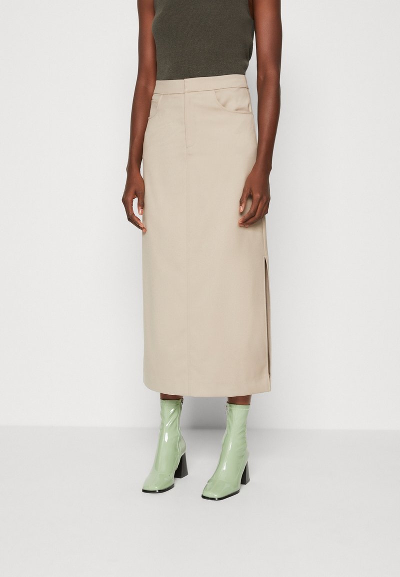 Beige midiklänning med sidoklipp, gjord av mjukt tyg. Kombinerad med glänsande gröna anklarstövlar med klackar.