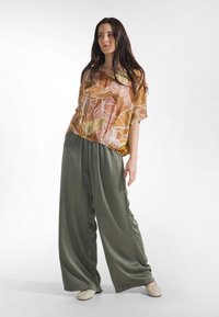 Kortærmet top med et farverigt løvmønster i orange, grøn og hvid, kombineret med løstsiddende, brede bukser i lys olivengrøn.