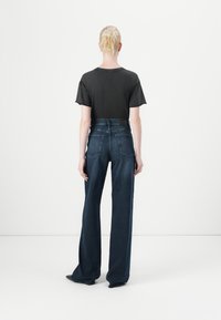 Tricou negru cu mânecă scurtă purtat cu blugi dark blue, cu talie înaltă. Blugii au o croială dreaptă și două buzunare la spate.