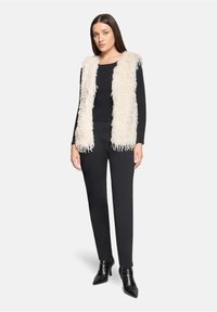 Kamizelka z futerkiem w kolorze kremowym, nałożona na czarną bluzkę z długim rękawem i dopasowane czarne spodnie. W połączeniu z czarnymi botkami na obcasie z zaostrzonym noskiem.