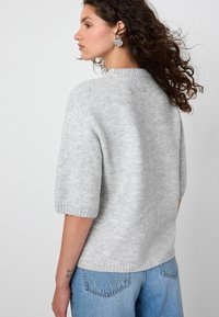 Maglione corto grigio chiaro a maniche corte con una texture morbida e collo a costine. La parte posteriore presenta un design semplice abbinato a jeans di denim.