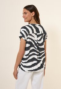 Korte mouw top van een lichtgewicht stof met een zwart-wit zebra-streep patroon. Losse pasvorm met opgerolde mouwen en een plooidetail aan de achterkant.