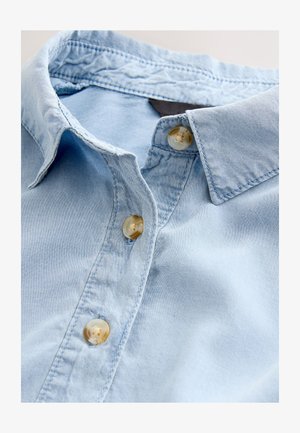 Šviesiai mėlyna džinsinio audinio marškiniai, turintys klasikinį apykaklę, du skaidrius mygtukus ir matomas siūles. Švelnios tekstūros, kasdieniško dizaino.