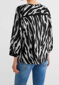 Blusa a strisce zebra nera e grigia con maniche lunghe, polsini abbottonati e scollatura rotonda. Realizzata in tessuto leggero con una vestibilità comoda.