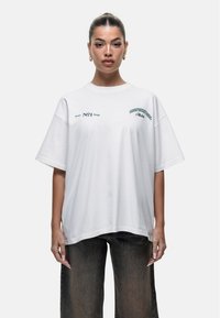 Biała, oversize T-shirta wykonana z miękkiej bawełny. Posiada zielony nadruk tekstu i logo z przodu. Luźny krój z szerokimi rękawami.