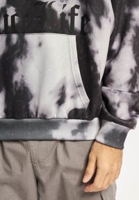 Hoodie v črno-sivi tie-dye z kenguru žepom, rebrastimi manšetami in širokim robom. Črn napis "Življenje" čez prsa.