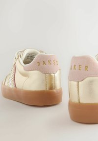 Kuldsete madalate tossude paar, millel on roosad nahast kannapadjad ja pruunid kummitaldad, kus on kuldsete tähtedega brändinimi "BAKER".