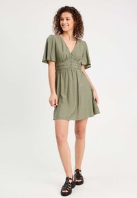 Robe vert olive avec des manches courtes à volants, décolleté en V et taille froncée, présentant une texture douce et une coupe décontractée.