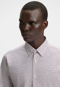Camicia bianca con bottoni, caratterizzata da un motivo testurizzato con accenti scuri, colletto classico e vestibilità sartoriale.