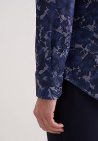 Koszula z długim rękawem w granatowo-szary kwiatowy wzór, wykonana z gładkiej tkaniny. Mankiety ozdobione dopasowanymi guzikami i szwami.