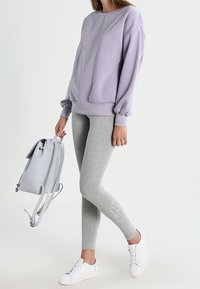 Lila överdimensionerad sweatshirt, grå leggings med logodetalj, vita sneakers och en ljusgrå ryggsäck. Slät tyg, avslappnad passform.
