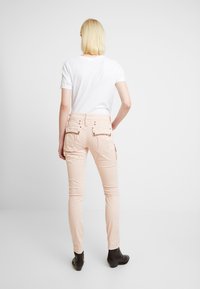 Kalhoty z měkké světle růžové látky se Slim fit, s kapsami na zadní straně zdobenými kamínky a mírně zúženými nohavicemi. Kombinováno s bílým tričkem.