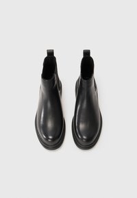 Par de botas Chelsea de cuero negro con punteras redondeadas y tiradores sobre un fondo blanco, vistas desde arriba.