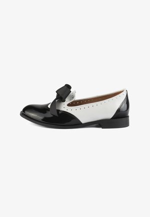 Chaussure plate en cuir noir et blanc avec une finition brillante, présentant un bout rond, un nœud décoratif et des détails perforés sur le côté.
