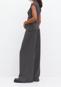 Top grigio a coste con maniche corte abbinato a pantaloni grigi a coste a gamba larga, caratterizzati da una texture morbida e una vestibilità rilassata. Scarpe marroni completano il look.