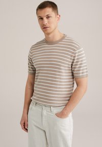 Beige, rövid ujjú csíkos pulóver, világos csíkokkal, kötött textúrával, kerek nyakkivágással. Világos színű farmernadrággal párosítva. Minimalista stílus.