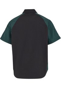 Camisa de manga corta con cuerpo negro y mangas raglán de color verde oscuro, que presenta un cuello clásico y una textura suave.