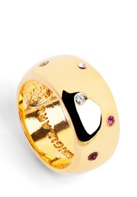 Goldfarbener, massiver Ring mit glatter Oberfläche, verziert mit farbigen Edelsteinen (pink, grün, lila) und einem schwarzen Akzent. Innerhalb mit dem Markennamen graviert.