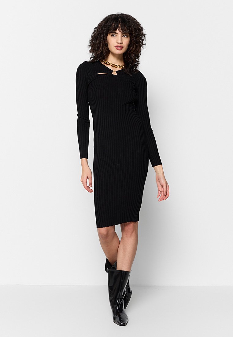 Vestido negro acanalado con mangas largas, presenta un corte frontal, largo midi y una silueta ajustada, combinado con botas negras hasta la rodilla.