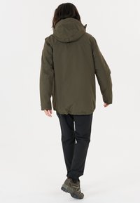 Olivgrön isolerad jacka med huva, med en något inblåst midja, lång ärm och slät yta; kombinerad med svarta byxor och skor.