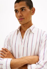 Λευκό πουκάμισο με γιακά, με κόκκινες και μπλε κάθετες ρίγες, με κουμπιά στο μπροστινό μέρος και ριμπ υφή σε κλασική γραμμή.