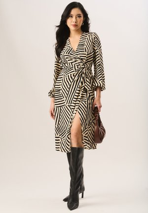 Long wrap dress featuring a beige and black striped pattern, deep V-neck, long sleeves, and a thigh-high slit. Paired with black knee-high boots.