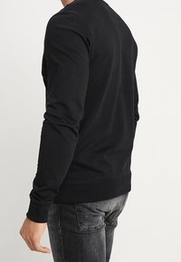 Felpa nera a maniche lunghe, in cotone, con scollo rotondo, polsini e orlo a coste, silhouette aderente, texture liscia, design minimale.