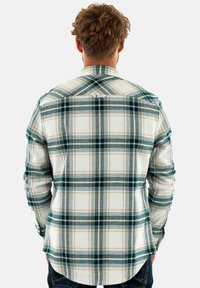 Camisa de franela a cuadros en verde, crema y marrón. Cuenta con un cuello button-down y una etiqueta en la parte posterior. Textura suave y mangas largas.