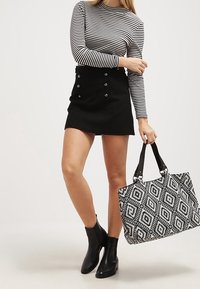 Svart minikjol med knappdetaljer, randig långärmad topp, svarta ankelstövlar och en stor toteväska med svart-vitt mönster.