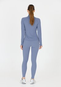Sportoutfit für Frauen in Hellblau, langärmliges Oberteil und enganliegende Leggings, aus glattem Material, mit hohem Kragen und nahtlosem Design.