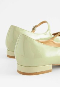 Glänzende hellgrüne Lacklederschuhe mit abgerundetem Zehenbereich, niedrigem Blockabsatz und Detail eines Knöchelriemens. Glatte Oberfläche mit sichtbaren Nähten.